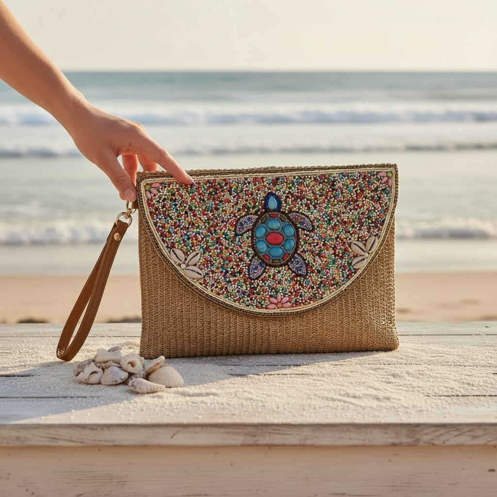 L and B Creations beaded turtle clutch with straw texture, seashell accents, and detachable wrist strap on a beach.