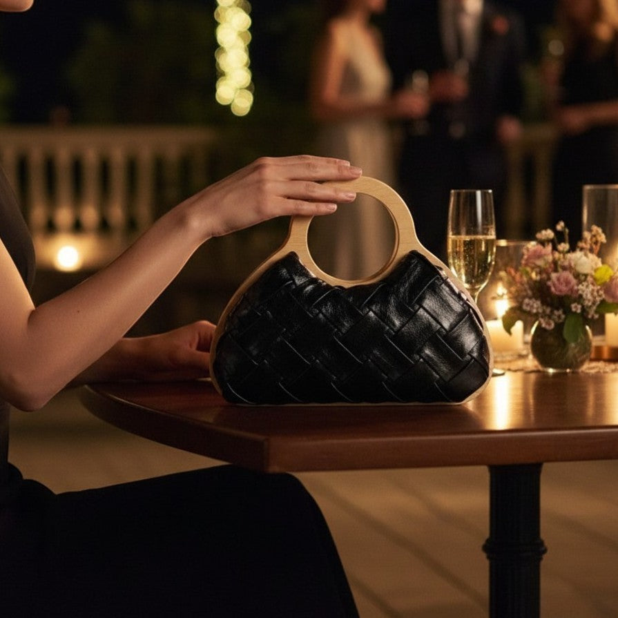 L and B Creations black woven fabric handbag with a round wooden handle held by a woman at an evening event