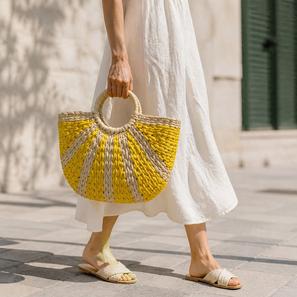 L and B Creations two-toned yellow and beige thick straw wicker handbag held by a woman in a white linen dress.